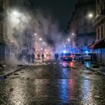 Smoke over a Paris boulevard at night with police lights during the October 2026 riots curfew