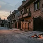 Empty street in a Multan housing society at dusk with a small memorial on the roadside